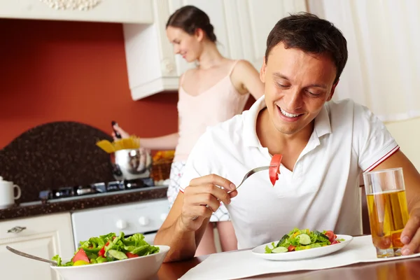 Mannen äter sallad med hustrun matlagning — Stockfoto