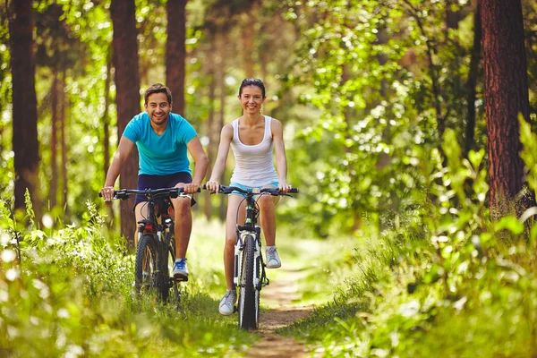 Man and woman riding bicycles in park — Stock Photo, Image