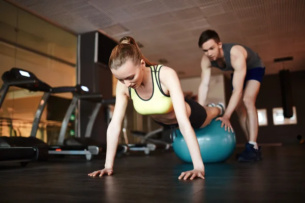 Woman doing push ups on ball with trainer — Stock Photo, Image