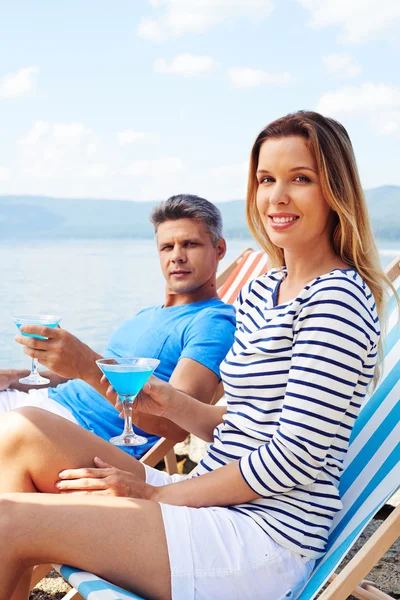 Frau und Mann mit Cocktails sitzen auf Liegestühlen — Stockfoto