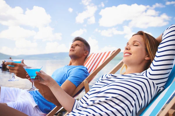 woman and man with cocktails sitting on deckchairs