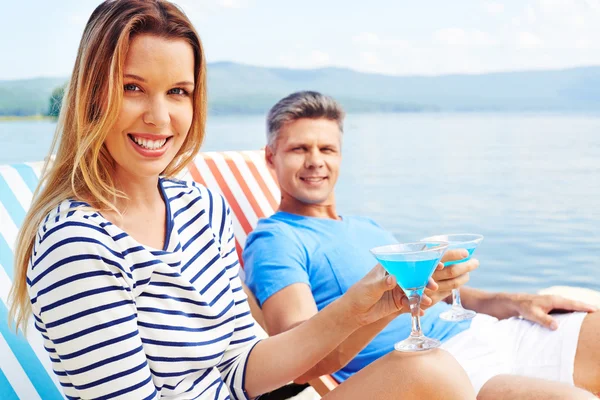 Vrouw en man met cocktails zittend op ligstoelen — Stockfoto