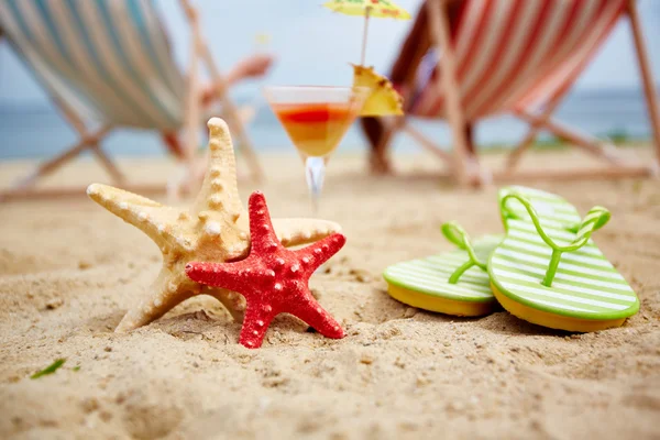 Морские звезды на пляже с коктейлем и шлепанцами — стоковое фото
