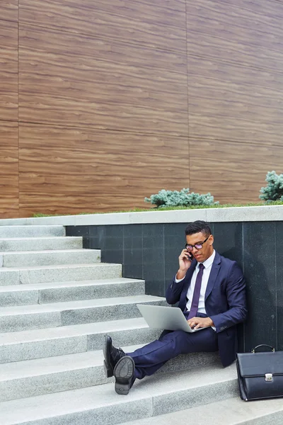 Businessman in suit speaking on cellphone and typing — Stock Photo, Image