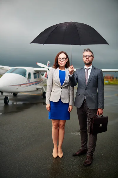 Compañeros de confianza bajo paraguas en el aeropuerto — Foto de Stock