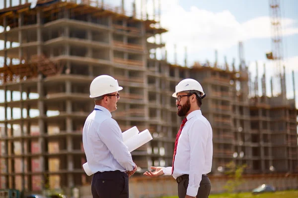 Hombres de negocios con cascos en frente de la construcción sin terminar — Foto de Stock