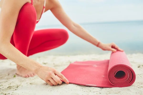 Donna tappetino svolgersi per lo yoga sulla spiaggia — Foto Stock