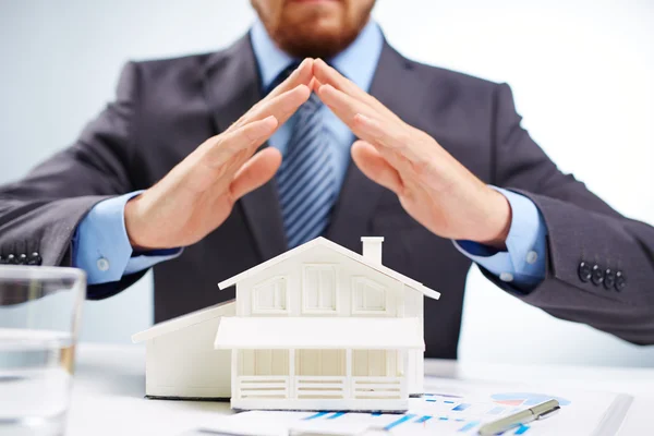 Businessman keeping palms over toy house — Stock Photo, Image