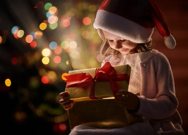 Mädchen in Weihnachtsmannmütze betrachtet Geschenk — Stockfoto