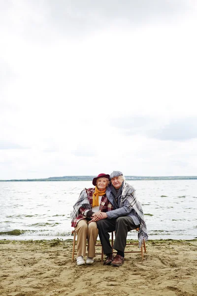 Щасливі літні люди, що сидять біля моря — стокове фото
