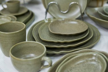 Masaya dizilmiş seramik tabaklar ve fincanlar, çeşitli boyutlarda yemek takımları, yakın plan renklendirme dokusu ve mutfak malzemelerinin zanaatkarlığı sergileniyor.