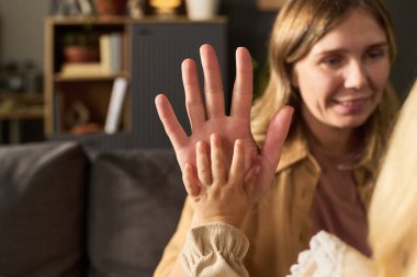 Kafkasyalı kadın avucuna beyaz bir çocukla dokunurken gülümsüyor, iki elini kaldırıyor ve birbirine bastırıyor, kapalı bir yerde oturuyor ve arka planı bulanık.