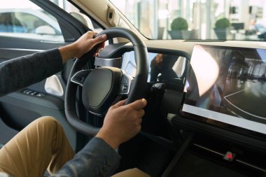 Beyaz, orta yaşlı, sürücü koltuğunda iki eliyle direksiyonda oturan bir adam modern galeride vites camına bakarken...