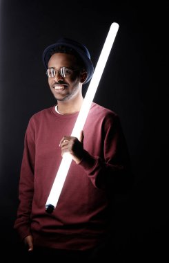 Elinde floresan lamba tutan ve karanlıkta kameraya gülümseyen Afrikalı Amerikalı bir adamın portresi.