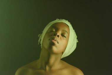 Beyaz başlıklı çıplak omuzlu genç, şehvetli bir kadının belden yukarı portresi. Gözleri koyu arka planda kapalı poz veriyor.