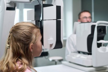 Modern tıp kliniğinde erkek optometrist işletim cihazı kullanırken ileri göz muayenesinden geçen beyaz kız ileri düzey göz hekimi.