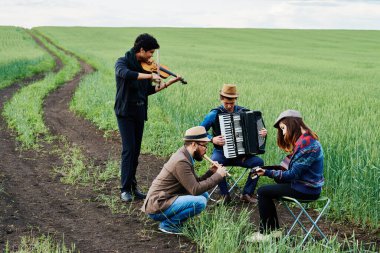 Yeşil alanda, keman, akordeon, gitar ve flüt çalarken ayakta ve oturarak, dışarıda konser veren genç, etnik çeşitlilikte müzisyenlerden oluşan bir grup, enstrümanlara odaklandı.