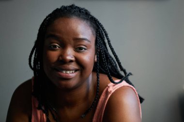 Afro örgülü, saçları kameraya gülümseyen çekici siyahi bir kadının orta boy portresi.