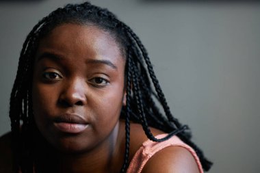 Saçları örülü, güzel siyah bir kadının kameraya bakarken çekilmiş yatay yakın plan portresi.