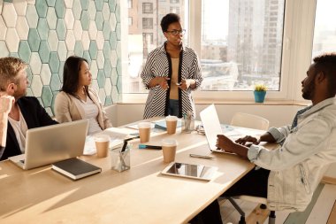 Multiethnic group of young businesspeople having meeting in conference room, stylish African American woman giving a speech