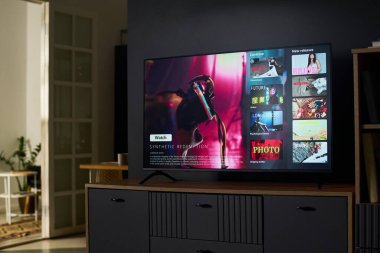 Modern düz ekran televizyon çeşitli film ve dizi küçük resimleriyle servis arayüzü sergiliyor, çağdaş oturma odasının içindeki dolapta duruyor