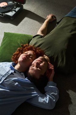 Dikey çekimde, genç aşıklar halının üzerinde uzanıyorlar. Kafaları dinleniyor. Kadın erkeğin kafasını nazikçe tutuyor.