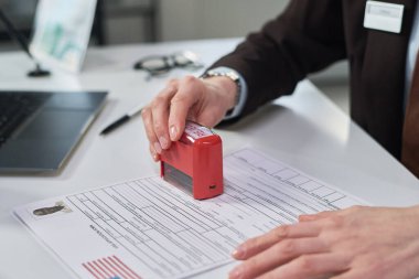 Vize işlemleri yapan kadın, kırmızı pul tutan, başvuru yapan kişinin fotoğrafını basan, Vize Merkezi masasında çalışan.