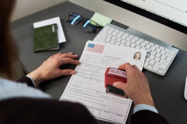 Vize merkezinde vize işlemlerini yapan beyaz bir kadın, bilgisayar monitörü, pasaport ve gözlük yakınındaki resmi belgede mühürleme reddedildi.