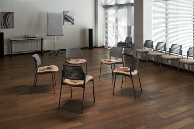 Koltukların üzerine broşürler yerleştirilmiş altı sandalyeli boş modern toplantı odası, arka planda doğal ışığa izin veren perdeli büyük pencereler, ters çevirme grafiği