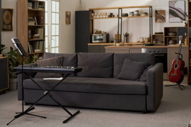 Mutfak tezgahına yaslanmış açık notalar ve akustik gitarla dijital klavyenin olduğu modern oturma odası, kitaplıklar ve arka planda görünen mutfak aletleri