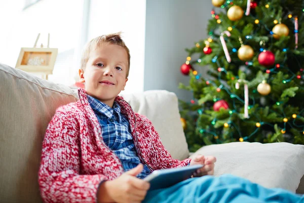 Chłopiec z touchpad siedzi przez Chrismas drzewo — Zdjęcie stockowe