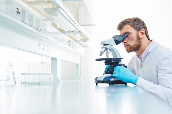man studying microbiological substance in microscope