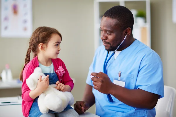 Flicka med nallebjörn tittar på klinikern — Stockfoto