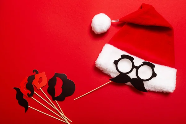 Red banner with a Santa hat with a white pompom and a face from glasses and mustache. A props for entertaining guests at a New Year corporate festive, speed dating or a karaoke party.