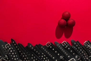Üç noel balosu, siyah deri pantolon askısı ve elleri ya da bacakları prangalı metal perçinler ve cinsel oyunlar için kırmızı pankart. BDSM deneği. Yetişkin oyuncak ürünleri veya seks mağazası reklamı için arka plan.