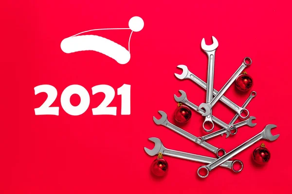 Kırmızı arka planda toplarla süslenmiş anahtarlardan yapılmış Noel ağacı. Aletli yeni yıl afişi. Sanayi bayramı konseptiyle yeni yılı kutlamak için mesaj atılacak bir kartpostal. 2021.