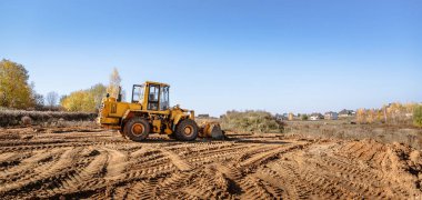 large yellow wheel loader aligns a piece of land for a new building. Preparation of the land for the auction. Leveling the landscape and adding sand for construction. Banner wallpaper. clipart