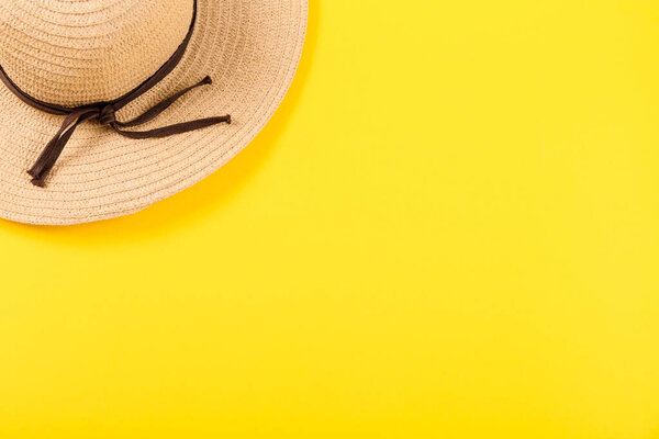 Top view on a retro straw hat on a yellow background. Summer concept. Minimalistic wallpaper for advertising a happy vacation on the sea or ocean or travel agency services with free place for text. Close-up.