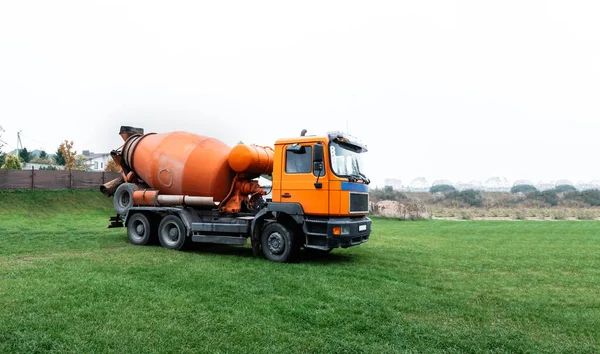 A large orange concrete mixer has arrived at the construction site. Special equipment transport for the delivery of building material - ready mixing cement. Business card, banner with copy space.