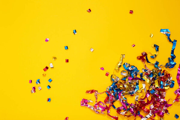 Colorful bright confetti and streamers on yellow background, top view. Copy space for text. Holiday mood, Christmas, New year, birthday or funny party.