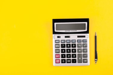 Gri ve siyah düğmeli büyük gümüş hesap makinesi ve sarı arka planda siyah kalem. Hesaplamaların kavramsal fotoğrafı, muhasebe, hesaplama, kar, zarar, metin yeri olan vergiler.