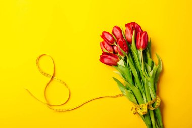 Kırmızı lale buketi ve 8 numaralı şerit şeklinde sarı arka planda fotokopi alanı ile birlikte. Fitness tebrik kartı. Uluslararası Kadın Günü ya da Anneler Günü. Dikiş hobisi. Çiçekçi.