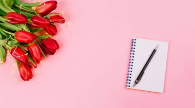 Pembe masa arkasında kırmızı lale ve kalem olan spiral not defterini aç. Metin için fotokopi alanı olan blog 'un tanıtımı ya da görselleştirilmesi için şablon. İş kartviziti. Sertifika modeli. Üst görünüm.