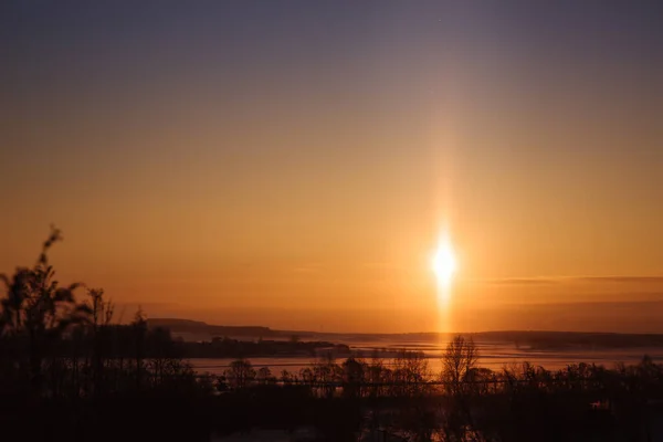 A rare atmospheric phenomenon is the solar light pillar. Beautiful morning winter landscape. Open space and fields at dawn. Good weather. Anomaly. Orange sun and sky. Environment and nature. Horizon.