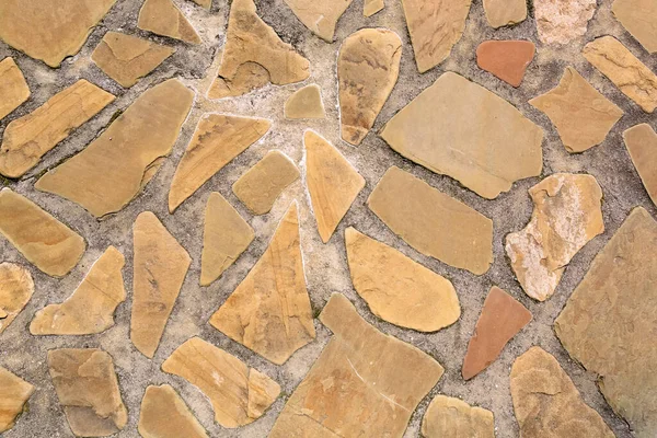 Cobblestone paved road. Curved stones are laid out in a path. Beige color. Fragment of the garden path decor. Textured background. A varied pattern. Handmade. Architectural element. Natural material.