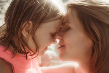 Güneşli bir gün, anne ve kızı sarılıp sohbet ediyorlar. Yaz tatili ya da hafta sonu plajda tatil. Çocukla yalnız bir annenin iletişim psikolojisi. Yakın plan. Mutlu bir yaşam tarzı anı.