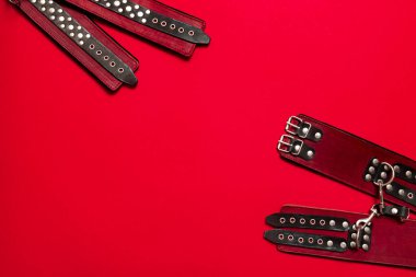 Siyah deri askılı kırmızı pankart ve kelepçeli eller ve bacaklar için metal perçinler ve seks oyunları. BDSM deneği. Yetişkin ürünleri ve seks oyuncakları mağazası reklamı için arka plan.