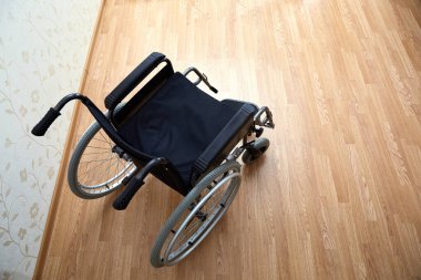 Evin arka planında geniş tekerlekleri ve manuel kontrolleri olan siyah tekerlekli boş bir sandalye. Bariyersiz bölge. Hiç kimse. Apartman dairesi. - Ev. Tıbbi araç gereç kiralama. Uzayı kopyala Hareket kabiliyeti devre dışı. Pankart.