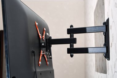 Dön TV ayraç LED ekran. Arkadan bak. X şeklinde kırmızı bağlayıcılar. Siyah renk. Çok düzlemli. Duvarda asılı. Güvenilir ve rahat bağlanma. Çocuk korumalı ve yuvarlanma korumalı. Metalik ekipman.