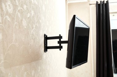 Dön TV ayraç LED ekran. Yan görüş. X şeklinde kırmızı bağlayıcılar. Siyah renk. Çok düzlemli. Duvarda asılı. Güvenilir ve rahat bağlanma. Çocuk korumalı ve yuvarlanma korumalı. Metalik ekipman.